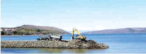 An excavator and trucks working on a rock breakwater