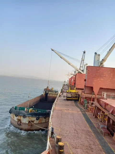A crane transferring material between a cargo ship and an alongside barge